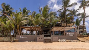 A beachfront hotel with a covered entrance, palm trees, and a clear sky.