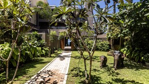 A pathway leading to a building with a tiled entrance, surrounded by lush greenery and a large elephant statue.