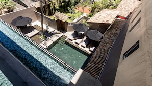 A rooftop pool area with lounge chairs and umbrellas, surrounded by a garden and buildings.