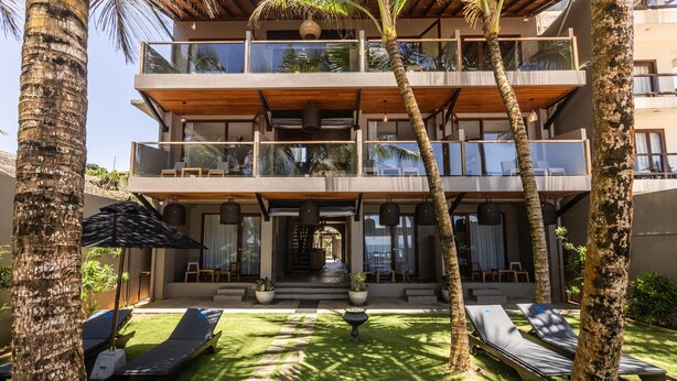 A multi-story building with a balcony, a lawn area with sun loungers, and palm trees.