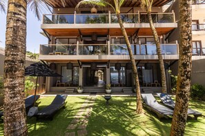 A multi-story building with a balcony, a lawn area with sun loungers, and palm trees. - BK Beach Boutique Hotel - Hikkaduwa (Dodanduwa)