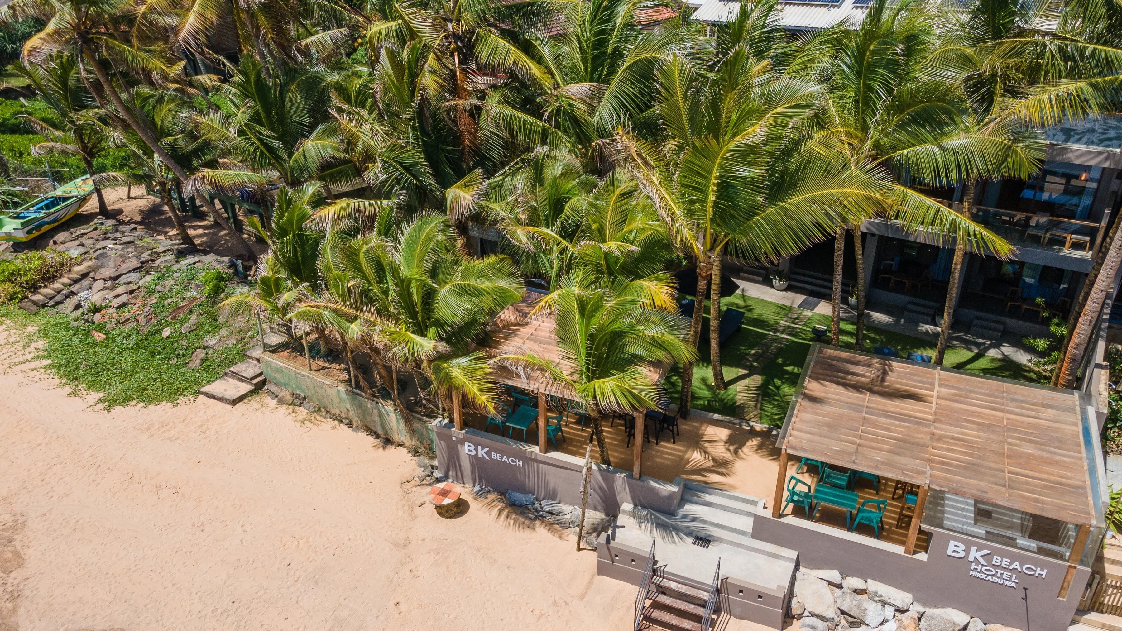 Un hôtel situé en bord de mer, agrémenté de palmiers, doté d’une plage de sable et d’un espace piscine.