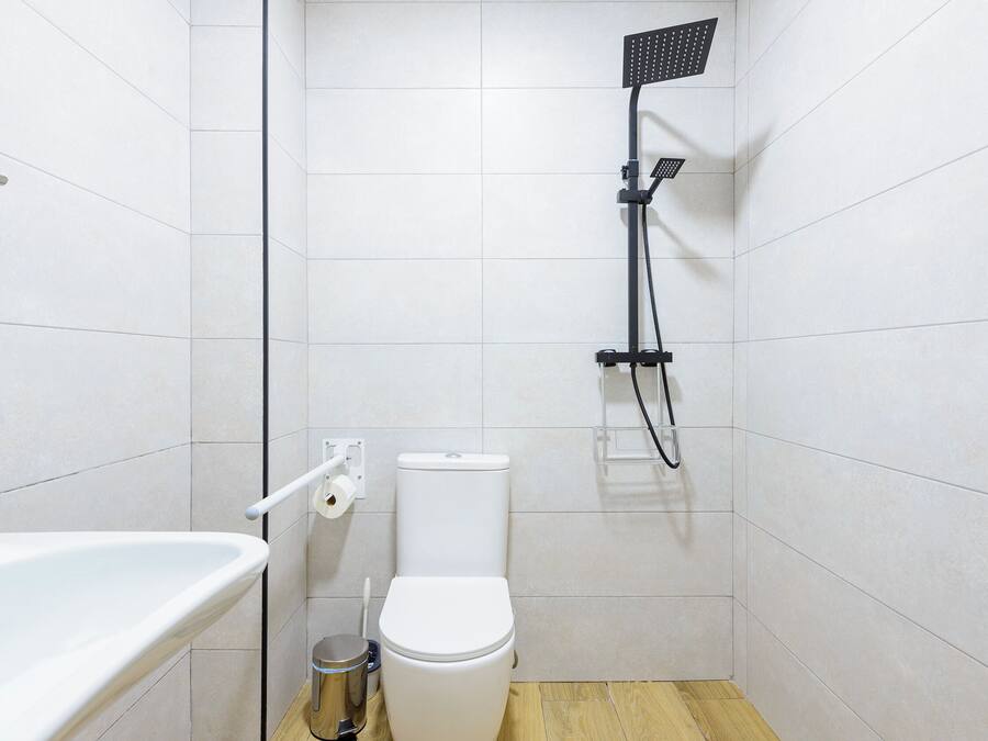 Un baño pequeño y moderno con inodoro blanco, cabezal de ducha y bañera blanca.