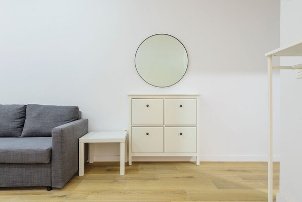 A room with a grey sofa, a small white table, and a white cabinet with two drawers.