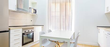 A modern kitchen with white cabinetry, a built-in oven, and a dining table with four chairs.