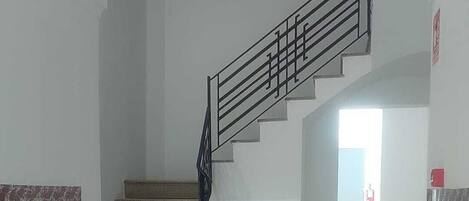 A staircase leading to an upper floor, with a handrail and a fire extinguisher on the wall.
