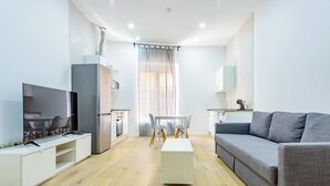 A modern living room with a flat-screen TV, a grey sofa, a white coffee table, a dining table with chairs, and a kitchen area with a refrigerator and microwave. -  Bieti Castellon (Castelló de la Plana)