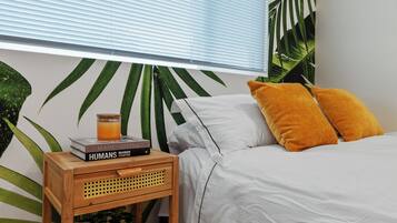 Une chambre avec un lit, une table de chevet sur laquelle se trouvent un livre et un verre de jus d’orange, et un mur orné d’une fresque représentant des feuilles tropicales.