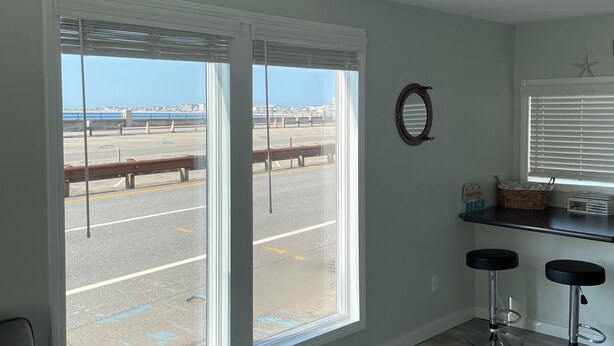 A room with large windows overlooking a parking area and a distant view of a bridge and buildings. There are two bar stools and a small shelf with items on it. - Ocean views from every window.  5min walk to the quiet end of the beach! (Hampton)