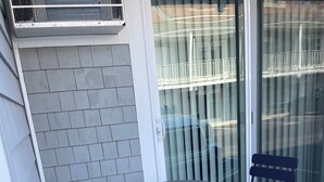 A patio with two chairs and a table, a white door, and a glass door with blinds. - Ocean views from every window.  5min walk to the quiet end of the beach! (Hampton)