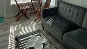 A living room with a grey sofa, wooden chairs, a small round table, and a view of an airport through large windows. - Ocean views from every window.  5min walk to the quiet end of the beach! (Hampton)
