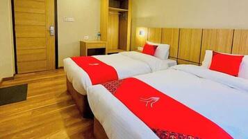 A hotel room with two beds, wooden flooring, a wardrobe, and a desk with a chair.