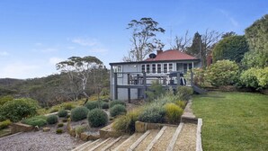 Ein zweistöckiges Haus mit Terrasse, umgeben von einem angelegten Garten mit verschiedenen Sträuchern und einem Kiesweg.