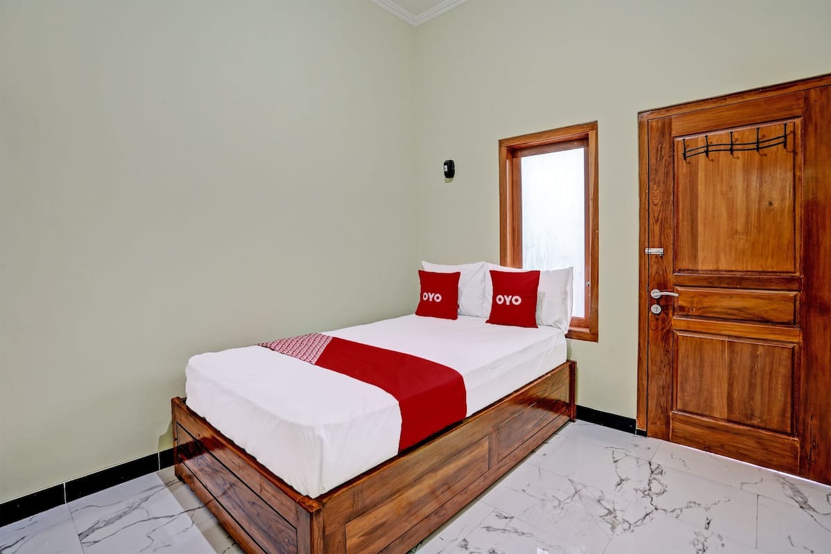 A neatly made bed with a white and red bedspread, a wooden headboard, and a wooden door with a coat rack.