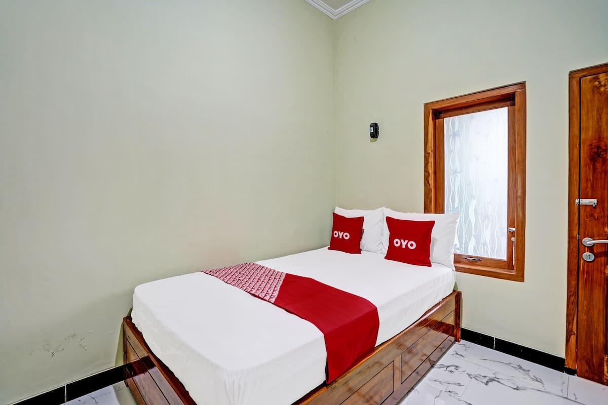 A single bed with a white and red bedspread, two red pillows, and a wooden headboard.