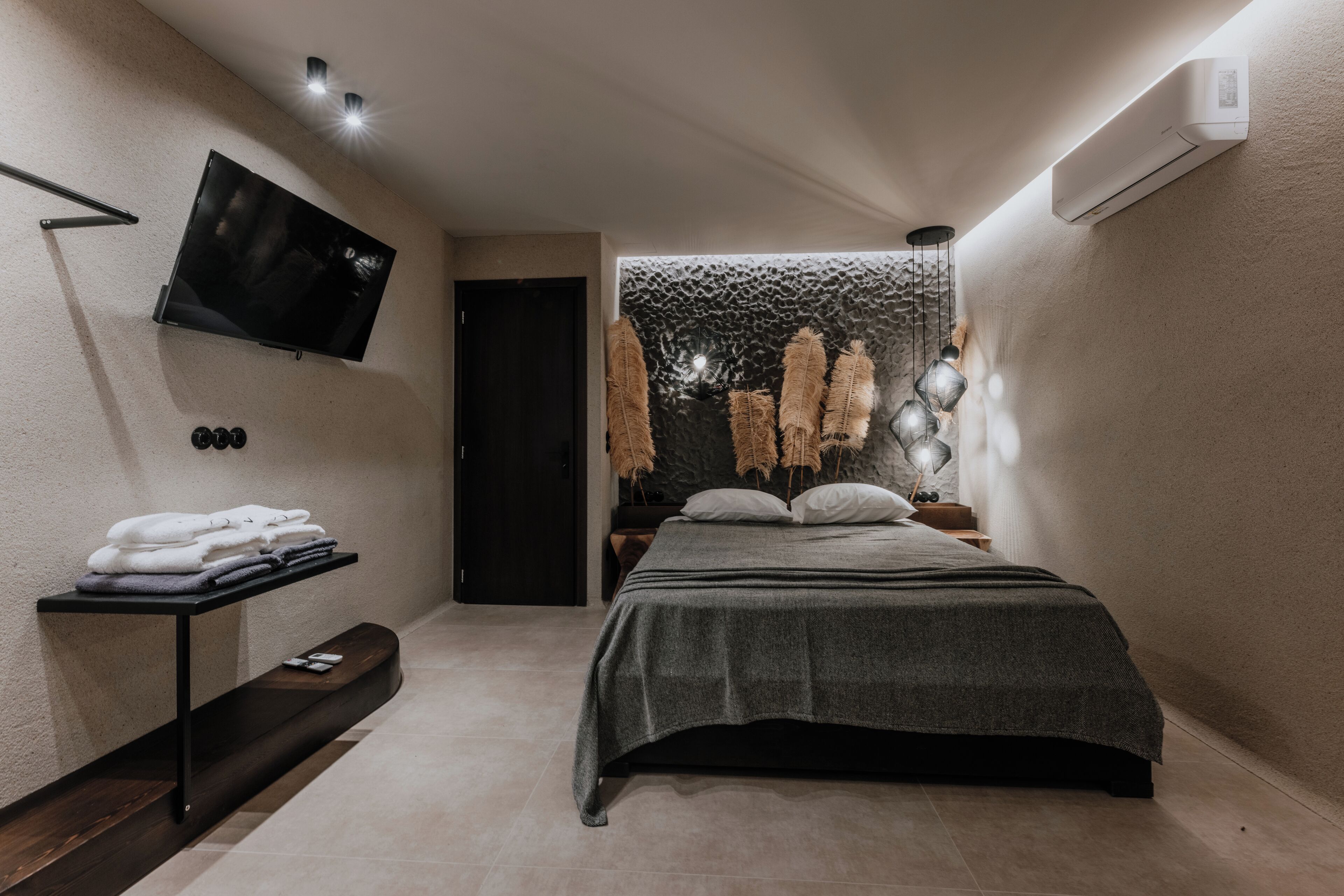 Une chambre à coucher moderne avec un lit, un téléviseur fixé au mur, une étagère avec des serviettes pliées et un élément décoratif mural.