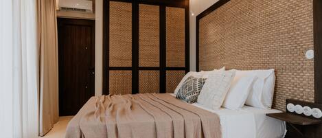 A bedroom with a bed, a wall-mounted air conditioner, a wooden door, and a textured wall.