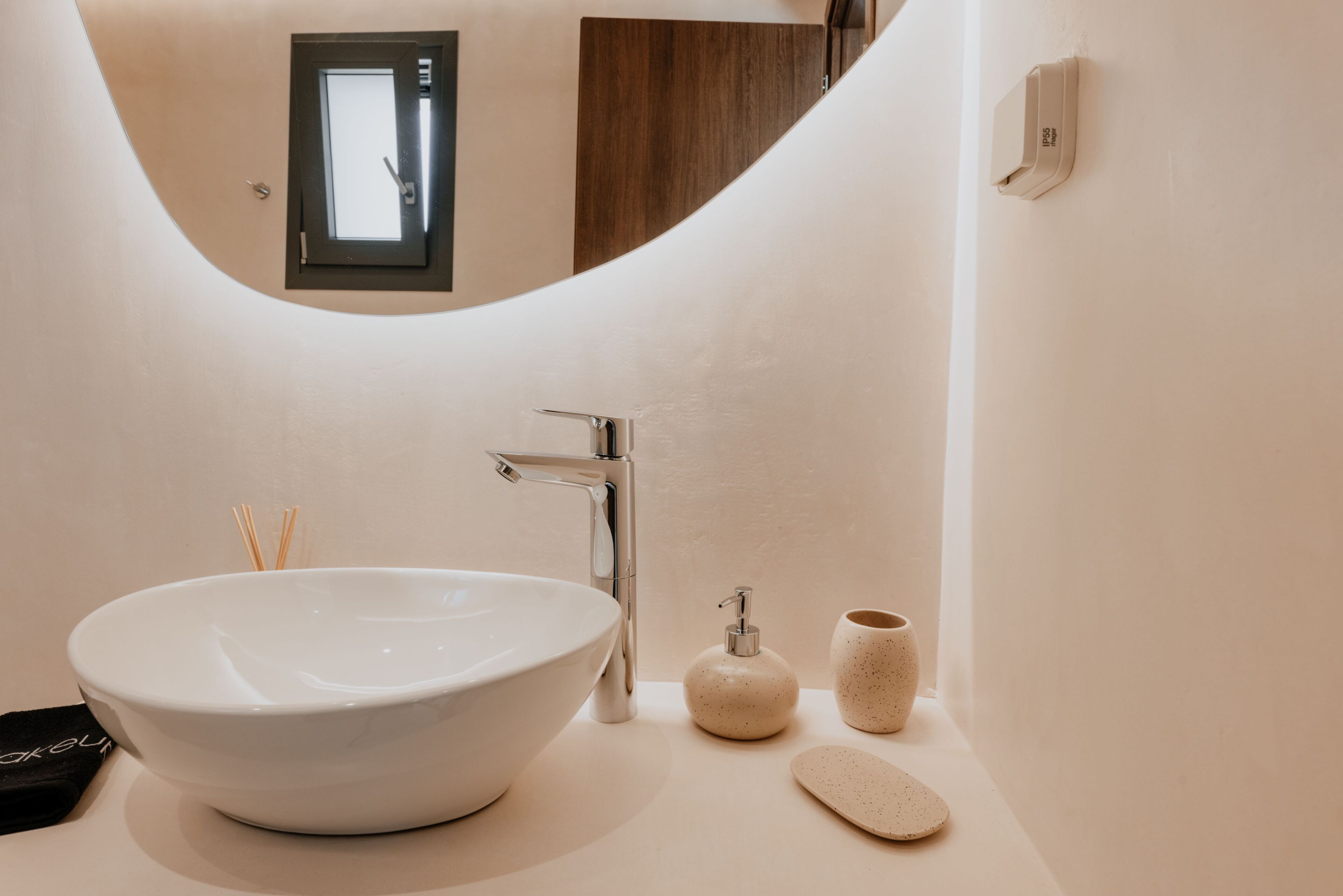 A modern bathroom with a large white sink, a chrome faucet, a soap dispenser, and a small ceramic cup.