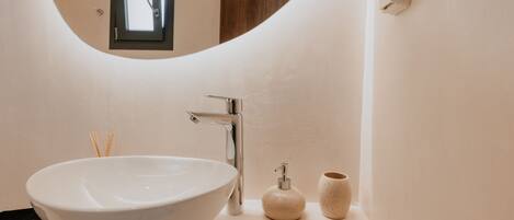 A modern bathroom with a large white sink, a chrome faucet, a soap dispenser, and a small ceramic cup.