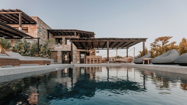 A modern pool area with a stone building, outdoor seating, and a covered patio. - Onym Curated Villas (Naxos)