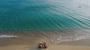 A beach with two people lying on the sand, facing the ocean. - Onym Curated Villas (Naxos)