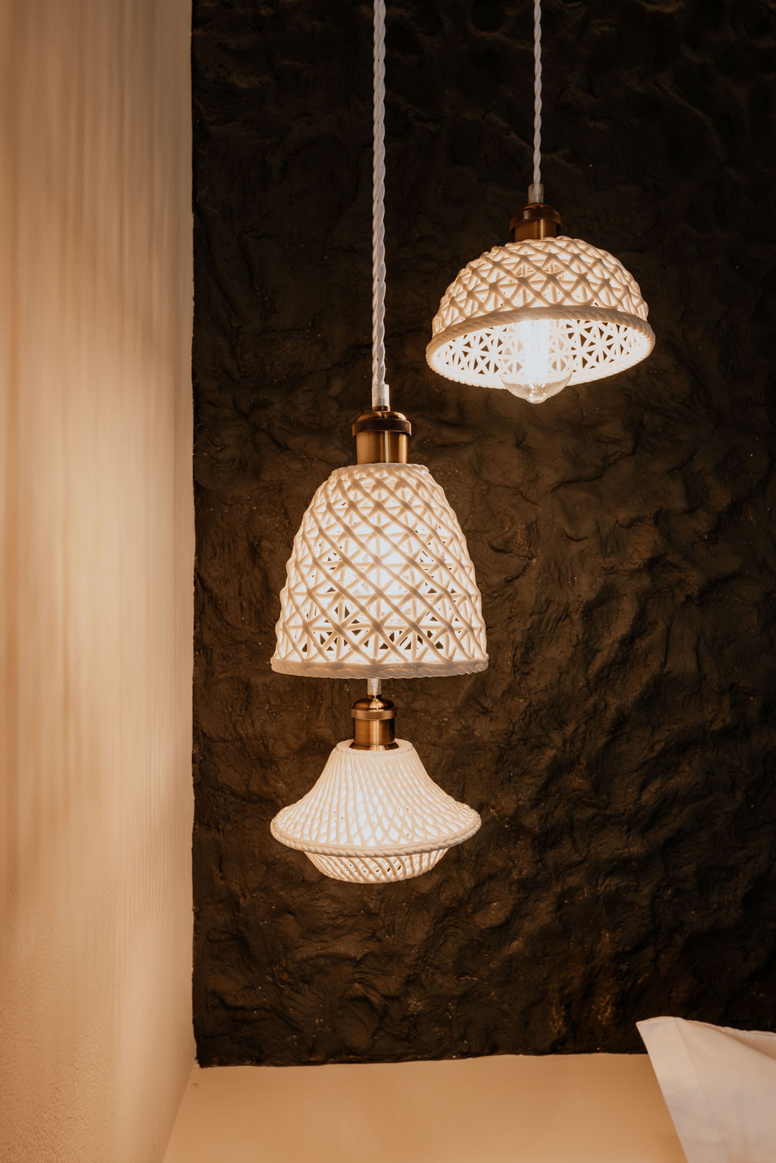 A room with a textured dark wall, a hanging white lamp with a geometric pattern, and a white curtain.