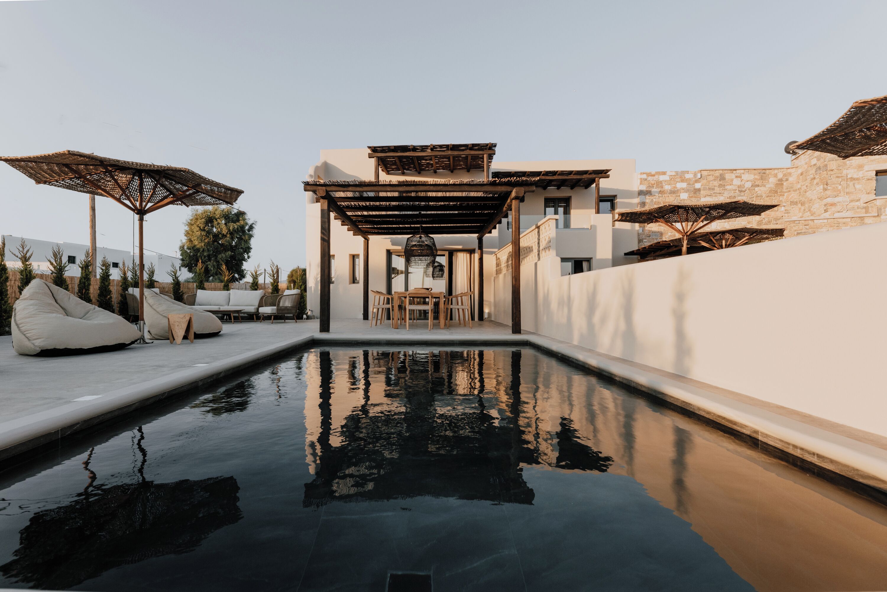 A swimming pool with a pergola and lounge chairs, surrounded by stone walls and umbrellas.
