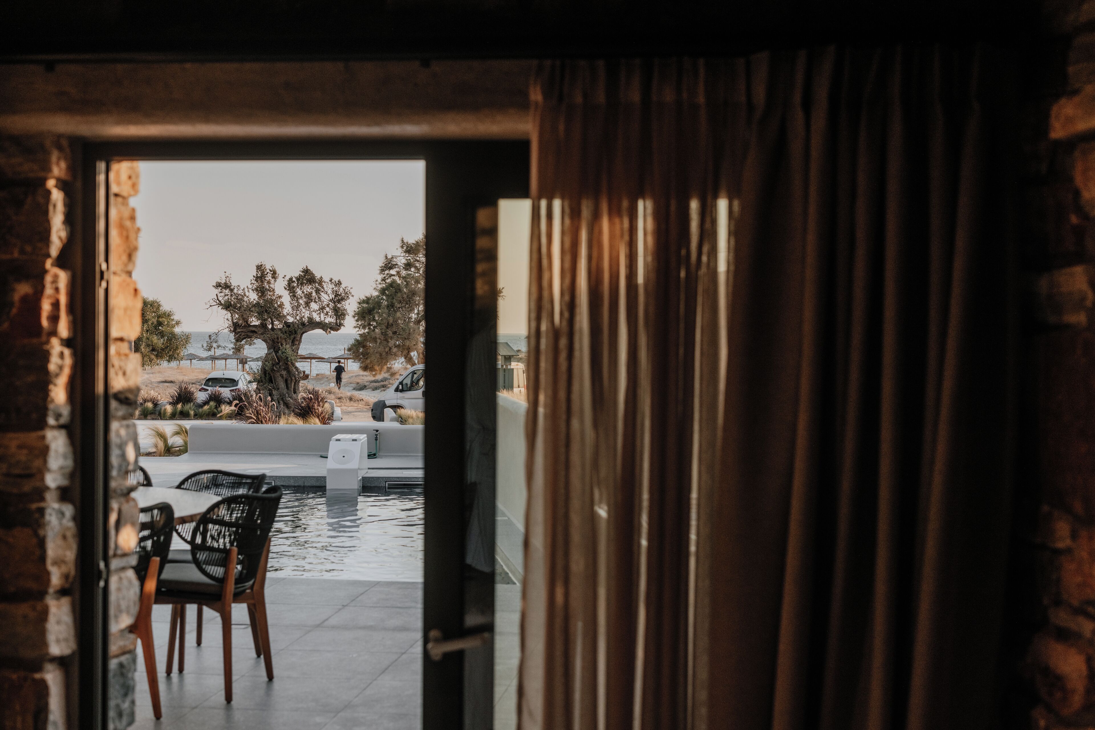 Une porte ouverte donne sur un espace piscine aménagé avec une table et des chaises.