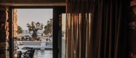Une porte ouverte donne sur un espace piscine aménagé avec une table et des chaises.