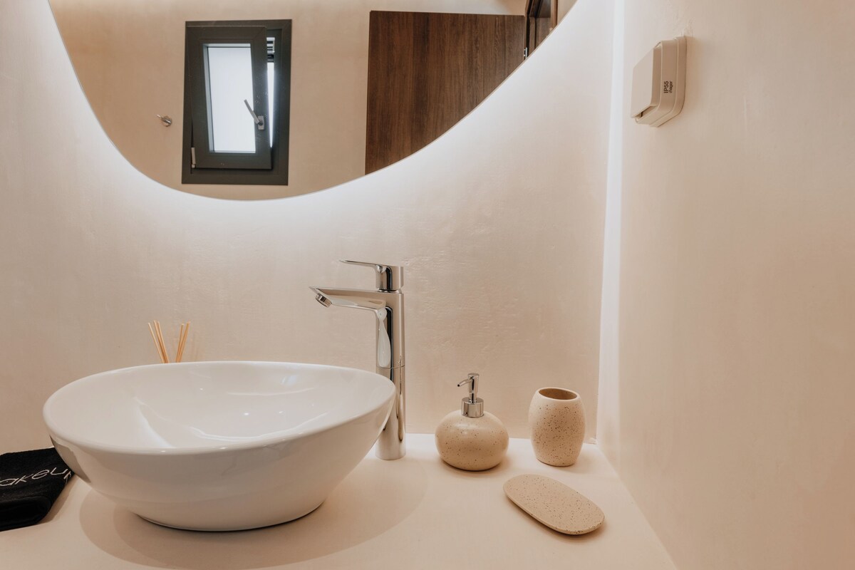 A bathroom with a large white sink, a modern faucet, a small soap dispenser, and a cup.