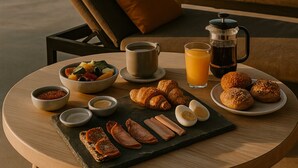 A breakfast table with croissants, eggs, and juice, overlooking a pool and outdoor seating area. - Onym Curated Villas (Naxos)