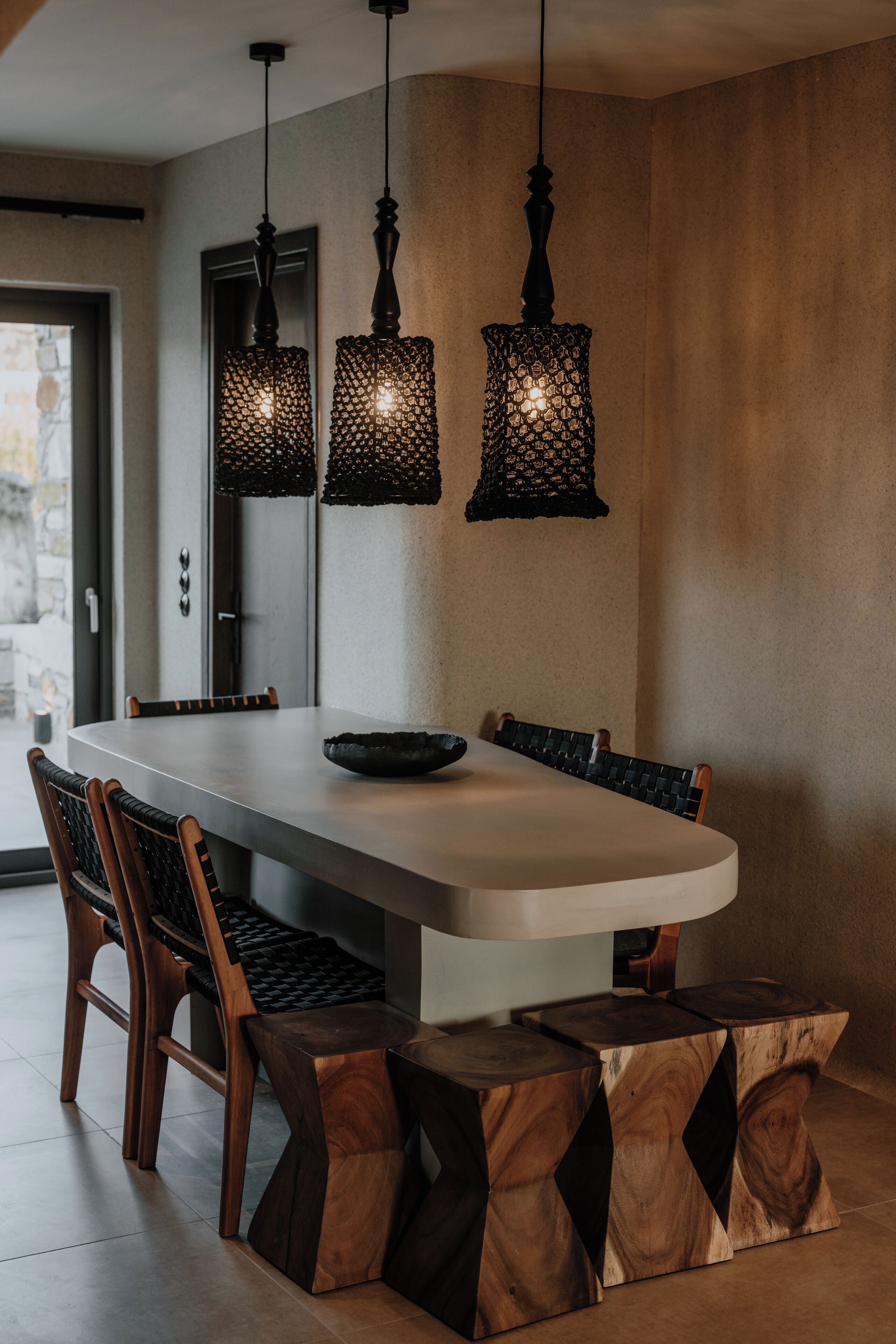 A modern dining area with a large table, wooden chairs, and unique hanging pendant lights.