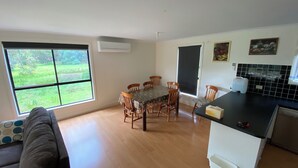 Een eetgedeelte met een tafel en stoelen, een keuken met een zwart aanrecht en een raam met uitzicht op groen.
