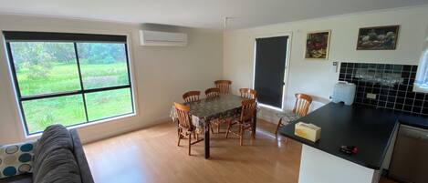 A dining area with a table and chairs, a kitchen with a black countertop, and a window with a view of greenery.