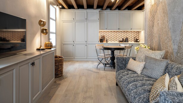 Una cocina moderna con armarios blancos, un comedor con mesa y sillas, y una sala de estar acogedora con un sofá estampado.