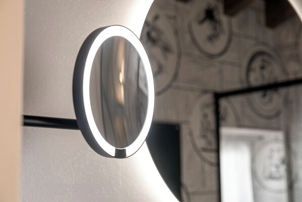 A circular mirror with a light around its edge, mounted on a wall with a patterned design. - CORLO Holiday Home (Lonato)