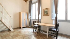 Une pièce avec une table en bois et deux chaises, un radiateur, un meuble et une fenêtre avec des rideaux.