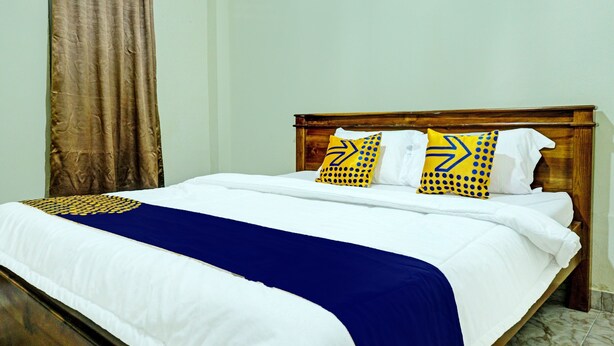 A neatly made bed with white and blue bedding, two pillows with yellow and blue patterns, and a wooden headboard.