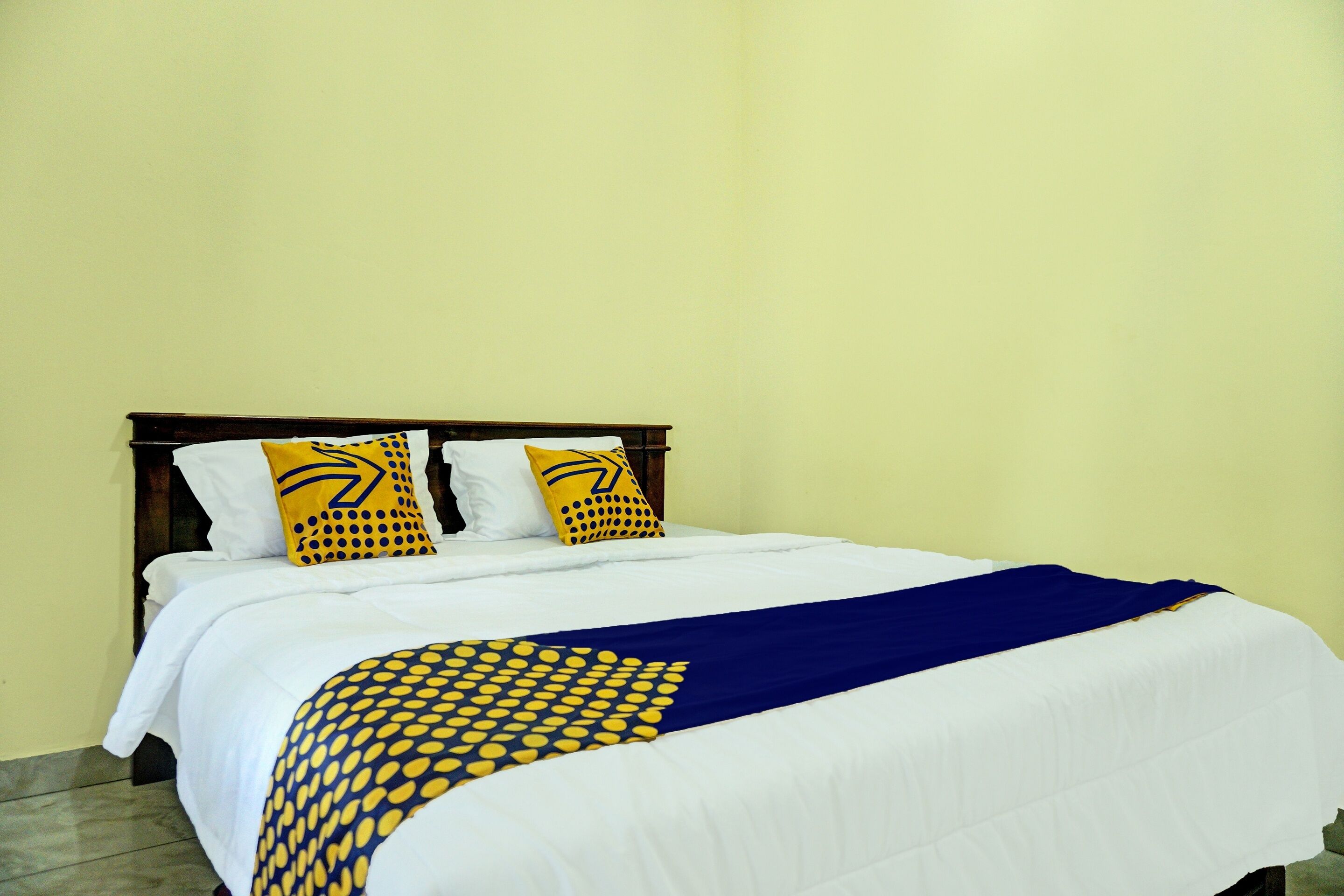 A neatly made bed with white bedding and two decorative pillows, a blue throw blanket, and a wooden headboard.