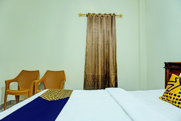 A room with a bed, two wicker chairs, a curtain, and a wooden nightstand with a pillow.
