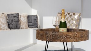 A wooden table with a bottle of champagne and two glasses, set against a white wall with patterned cushions. - Luxury Ocean View holiday home with sea view and shared pool (Corralejo)