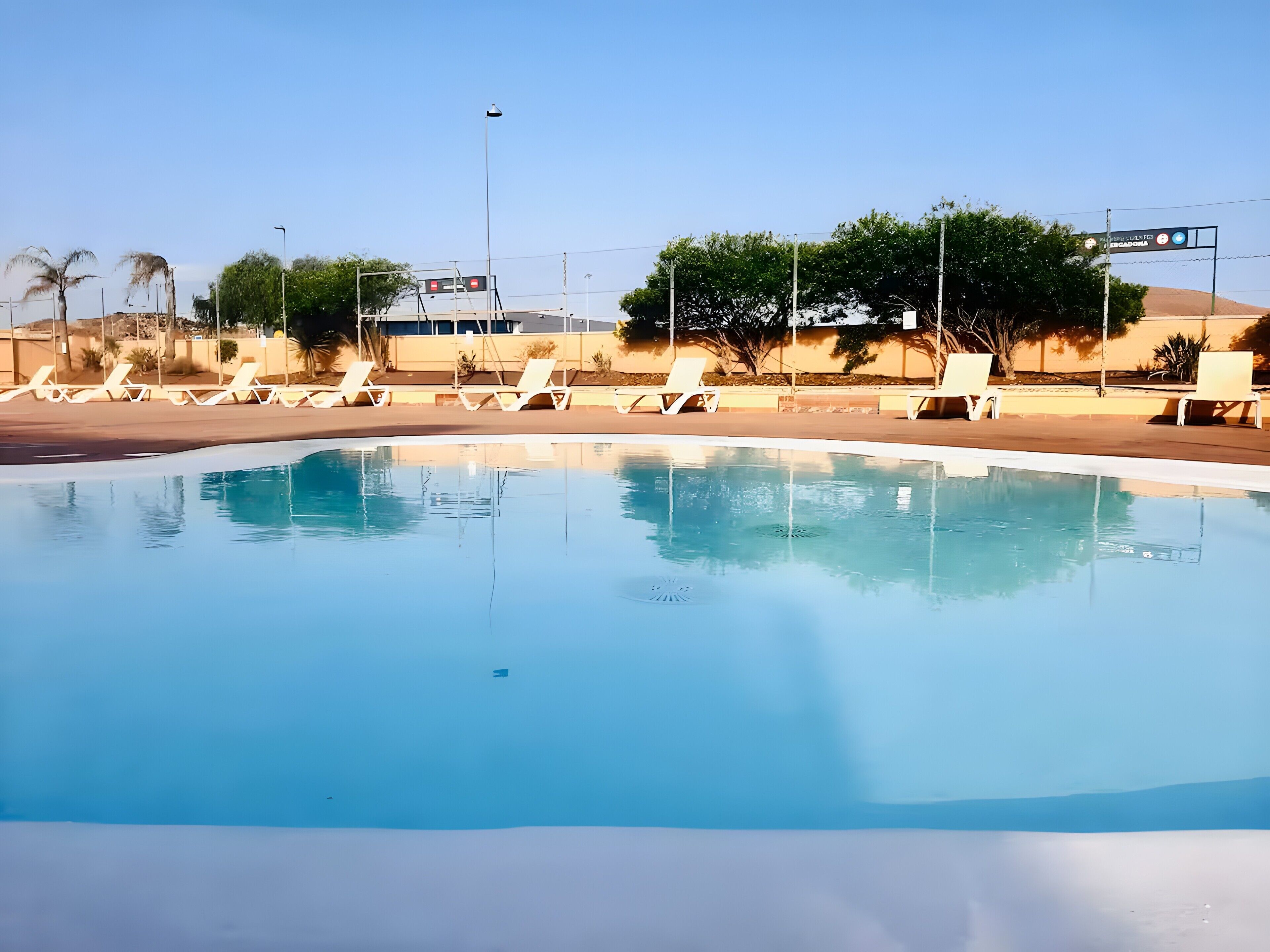 Una piscina con sillas de descanso, cielo despejado y un cartel que indica un lugar.