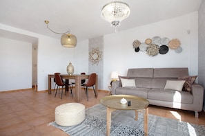 Ein Wohnzimmer mit einer Couch, einem runden Couchtisch, einem Esstisch mit Stühlen, einer Chandelierleuchtre und Wanddekoration.