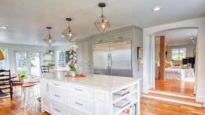 A modern kitchen with white cabinetry, a large island, and pendant lighting. - Hermes Haven Beach House - w/ Hot Tub, Blocks to beach (Encinitas)