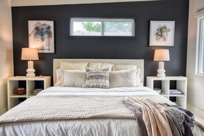 Een slaapkamer met een groot bed, twee nachtkastjes met lampen, en kunstwerken aan de muur.