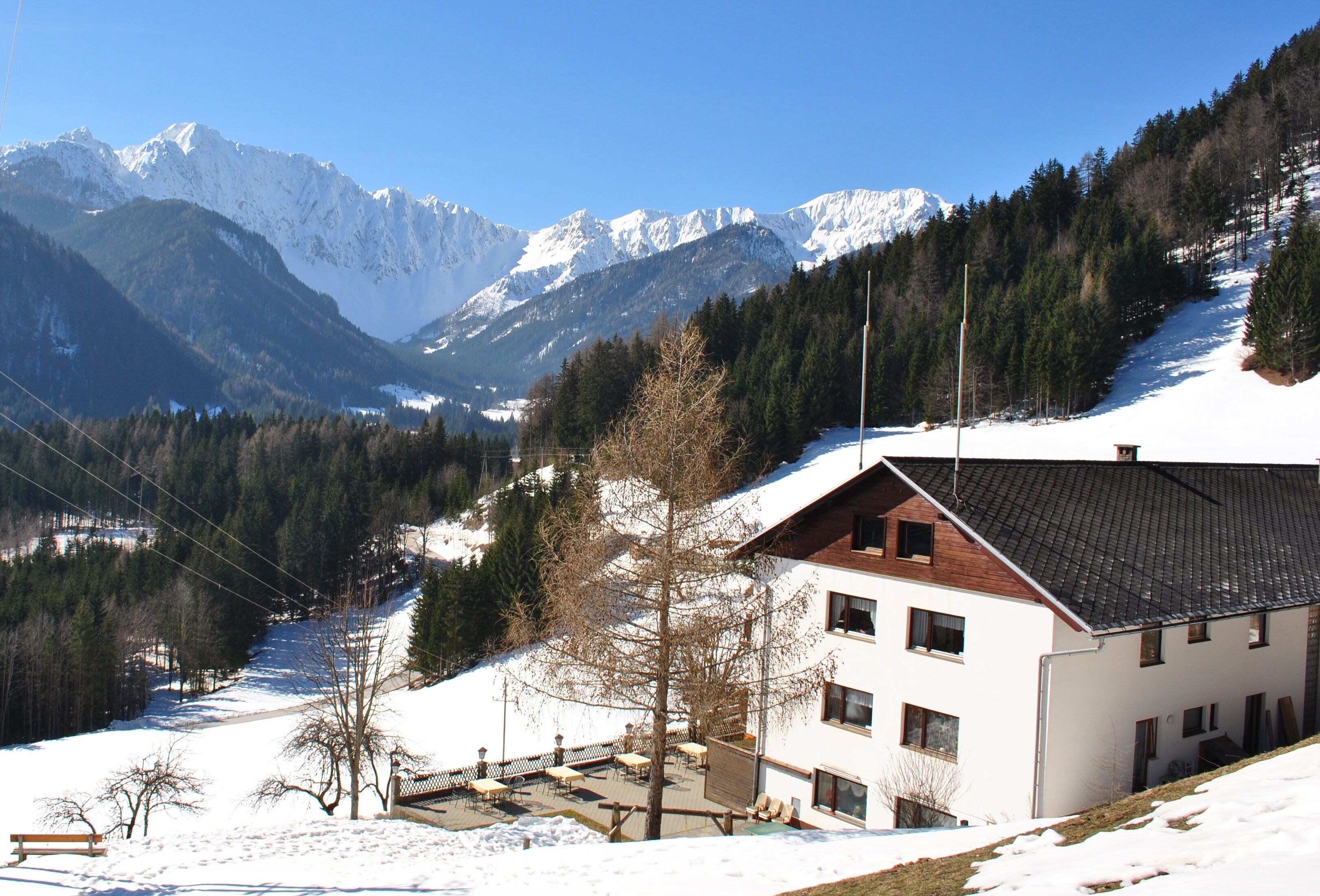 A two-story building with a sloped roof, situated on a snow-covered hillside with a view of snow-capped mountains in the background.
