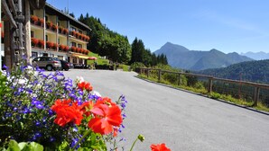 A hotel with balconies adorned with flowers, a paved road, and mountains in the background. - Bed&Breakfast Lausegger (Ferlach)