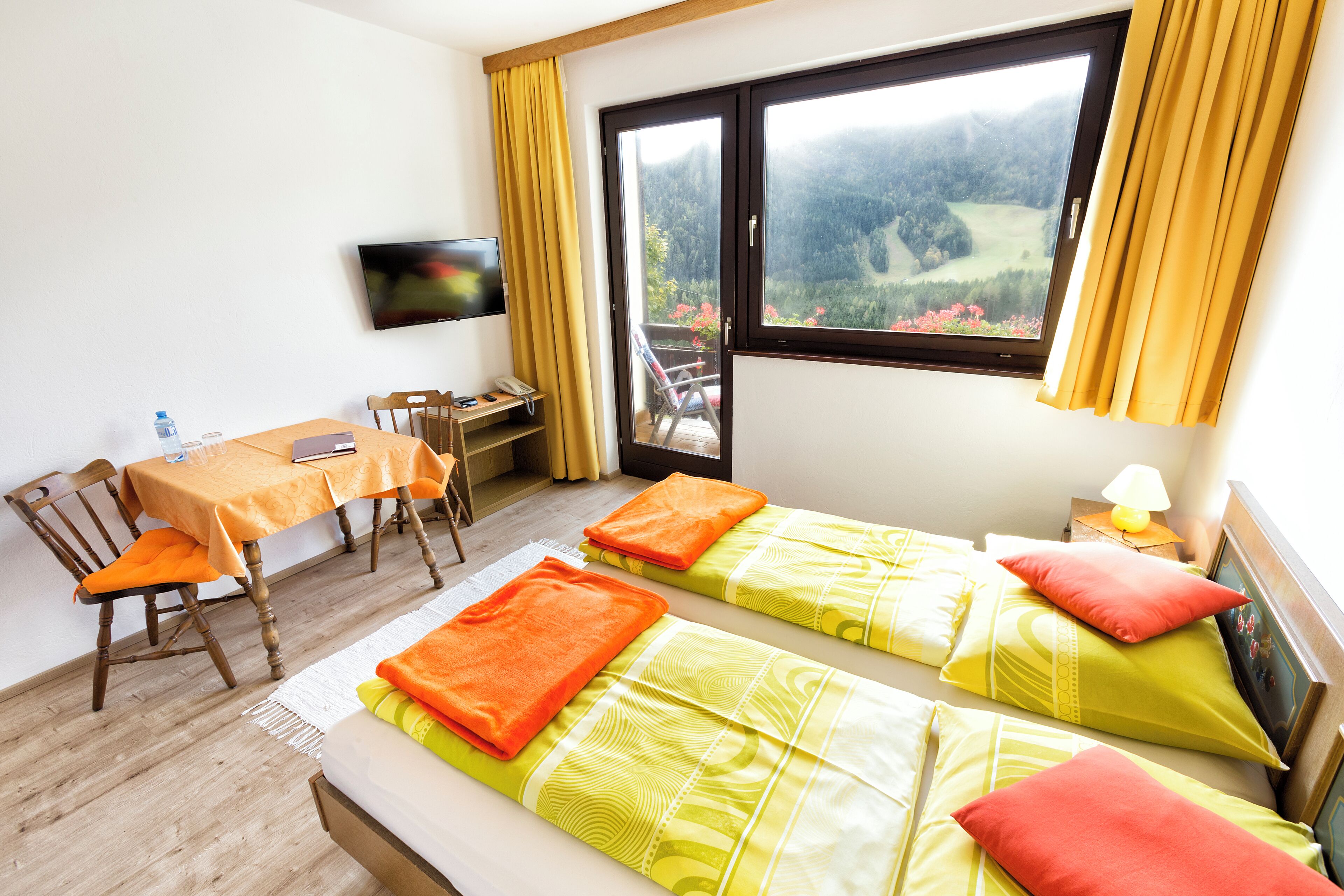 Habitación de hotel con dos camas, un escritorio, una silla, un televisor y una ventana con vistas a un bosque.