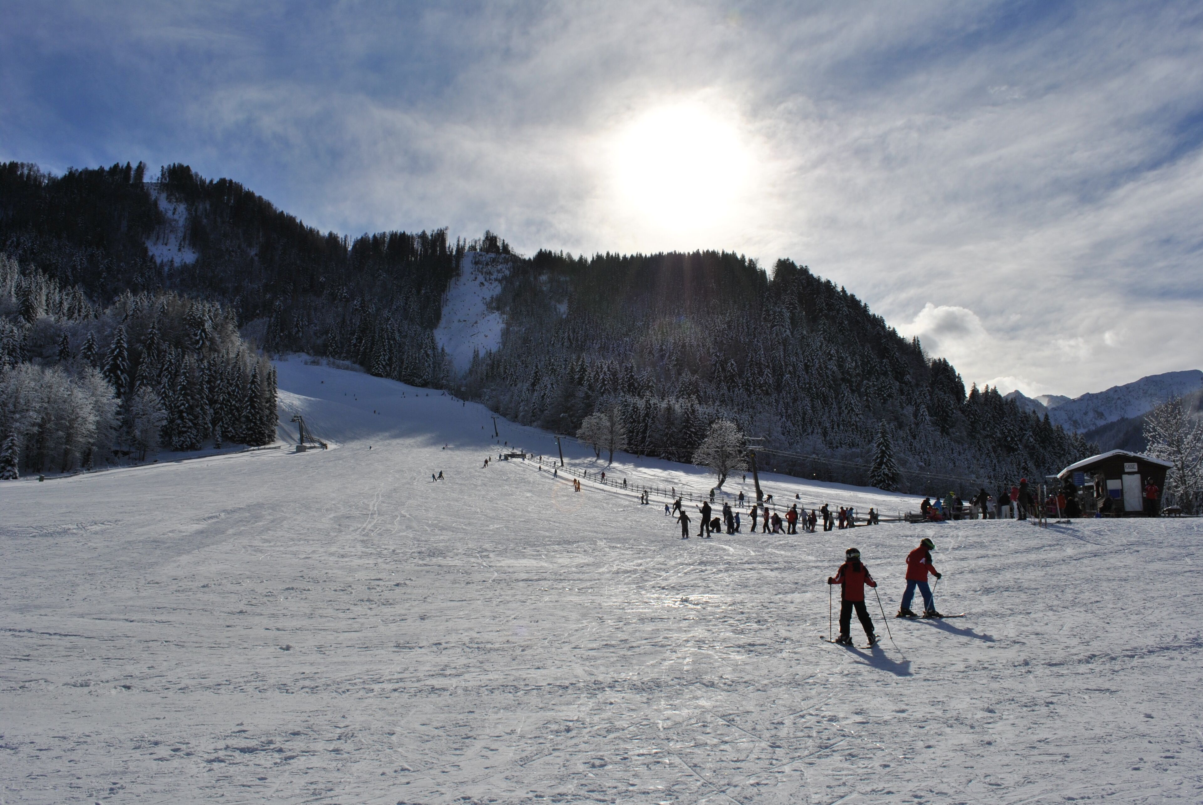 Une piste de ski enneigée, avec des skieurs et un chalet en arrière-plan.