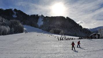 Une piste de ski enneigée, avec des skieurs et un chalet en arrière-plan.